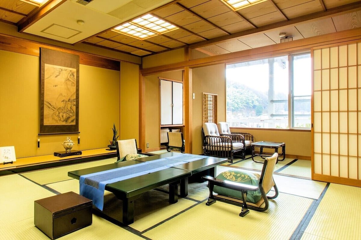 A tatami mat room with a tatami mat table, chairs, and a traditional Japanese sliding door.