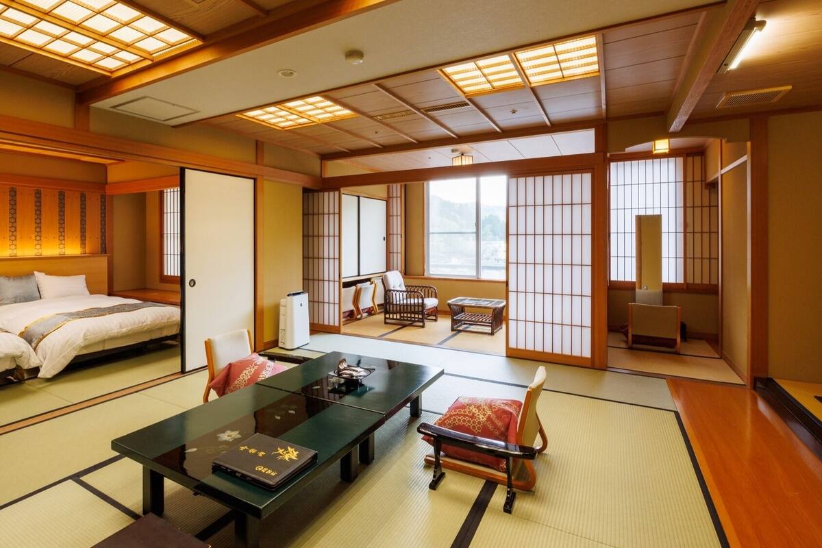 Ein traditioneller japanischer Raum mit Tatami-Bodenbelag, einem niedrigen Tisch mit einem Laptop und einem Bett mit einem Holz-Kopfstück.