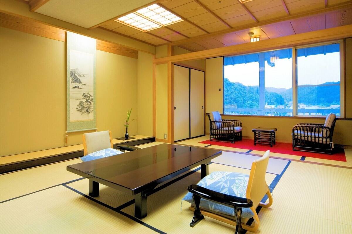 Ein Raum mit Tatami-Matten, einem niedrigen Tisch, Stühlen, einem großen Fenster mit Aussicht und einem traditionellen japanischen Wandbild.