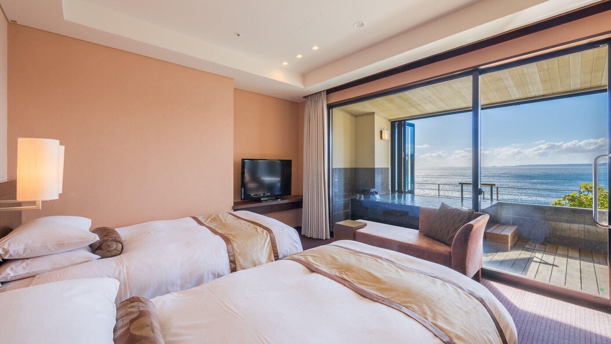Ein Hotelzimmer mit zwei Betten, einem Fernseher, einem Balkon mit Meerblick und einem großen Fenster.