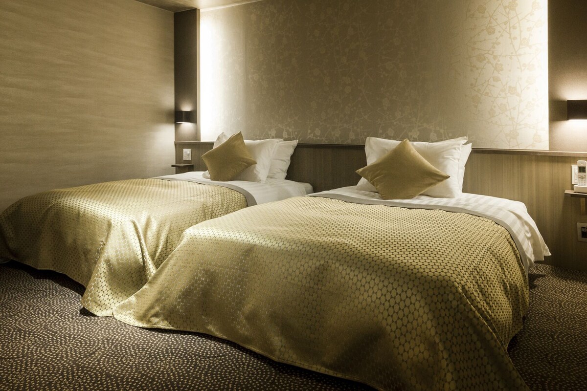 A hotel room with two beds, a nightstand, and a wall-mounted phone.