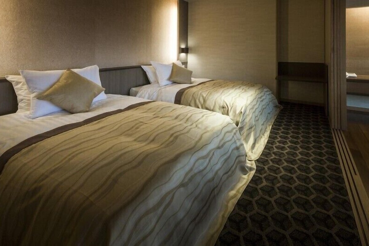 A hotel room with two beds, a patterned carpet, and a wall-mounted light fixture.