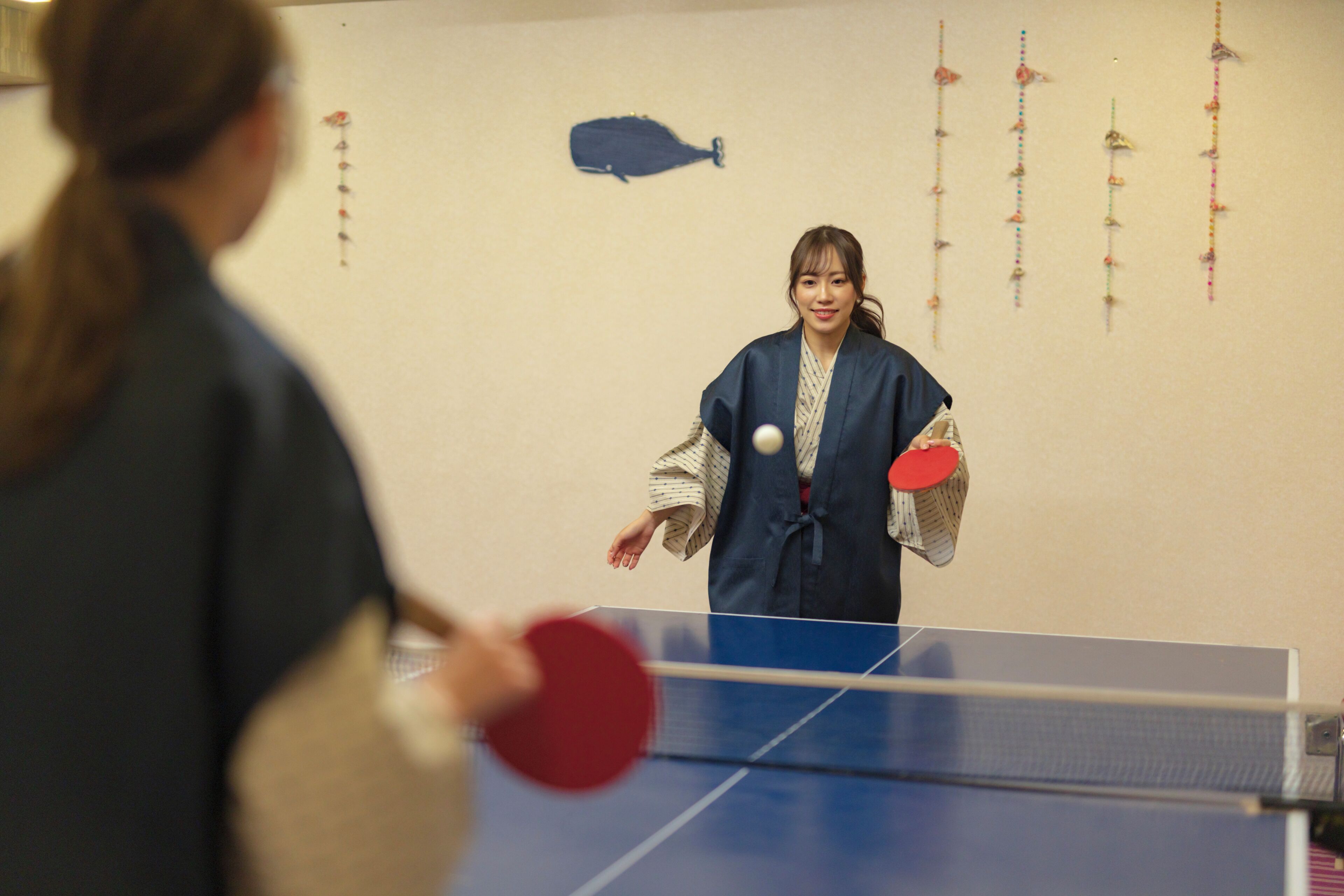 A table tennis table with a net in the middle, a person in traditional attire holding a paddle, and another person in the foreground.