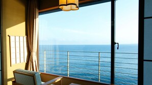 A room with a large window overlooking the ocean, a small table, a chair, and a hanging light fixture. - Inatori-Ginsuiso (Higashiizu)