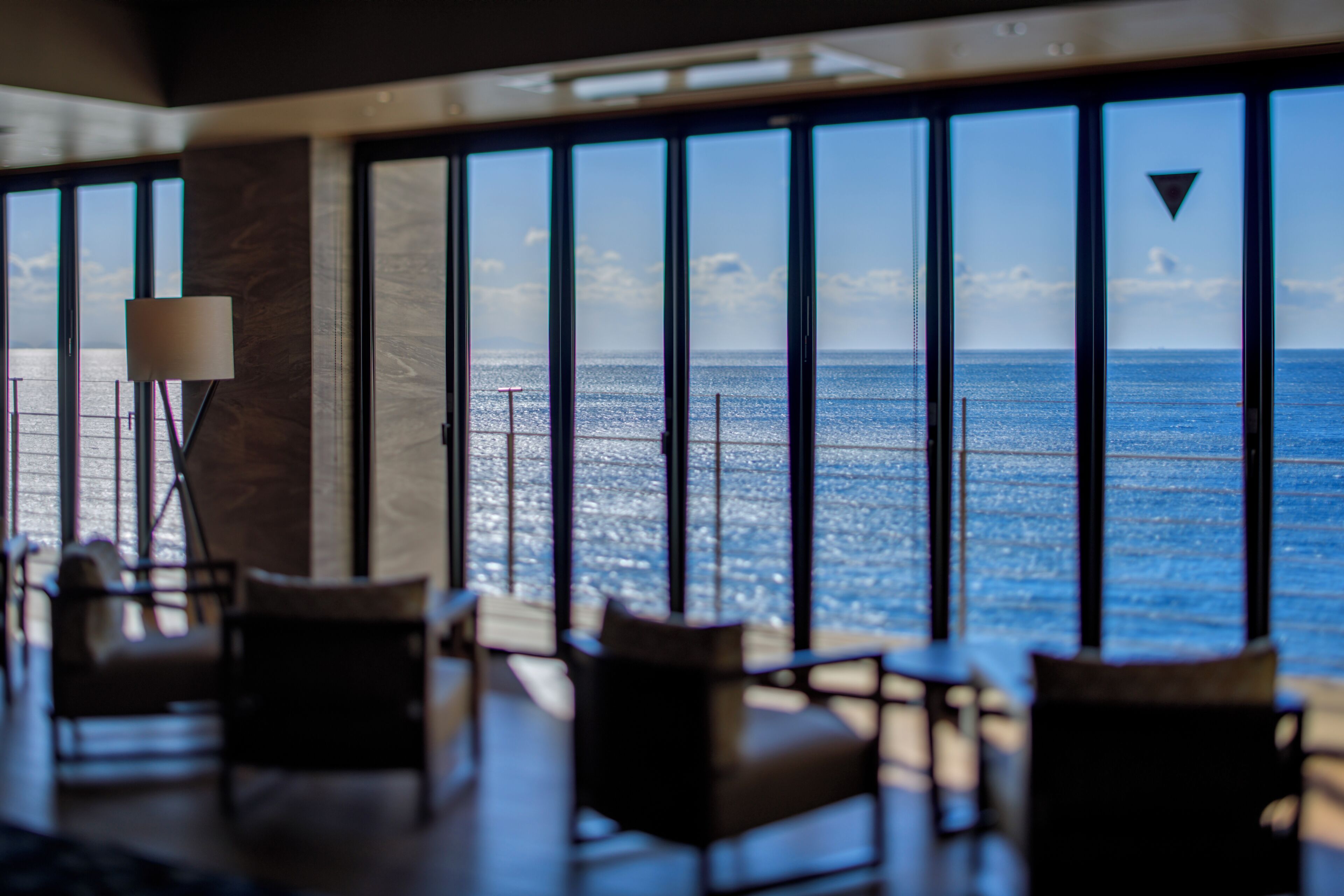 A room with large windows overlooking the sea, furnished with chairs and a table.