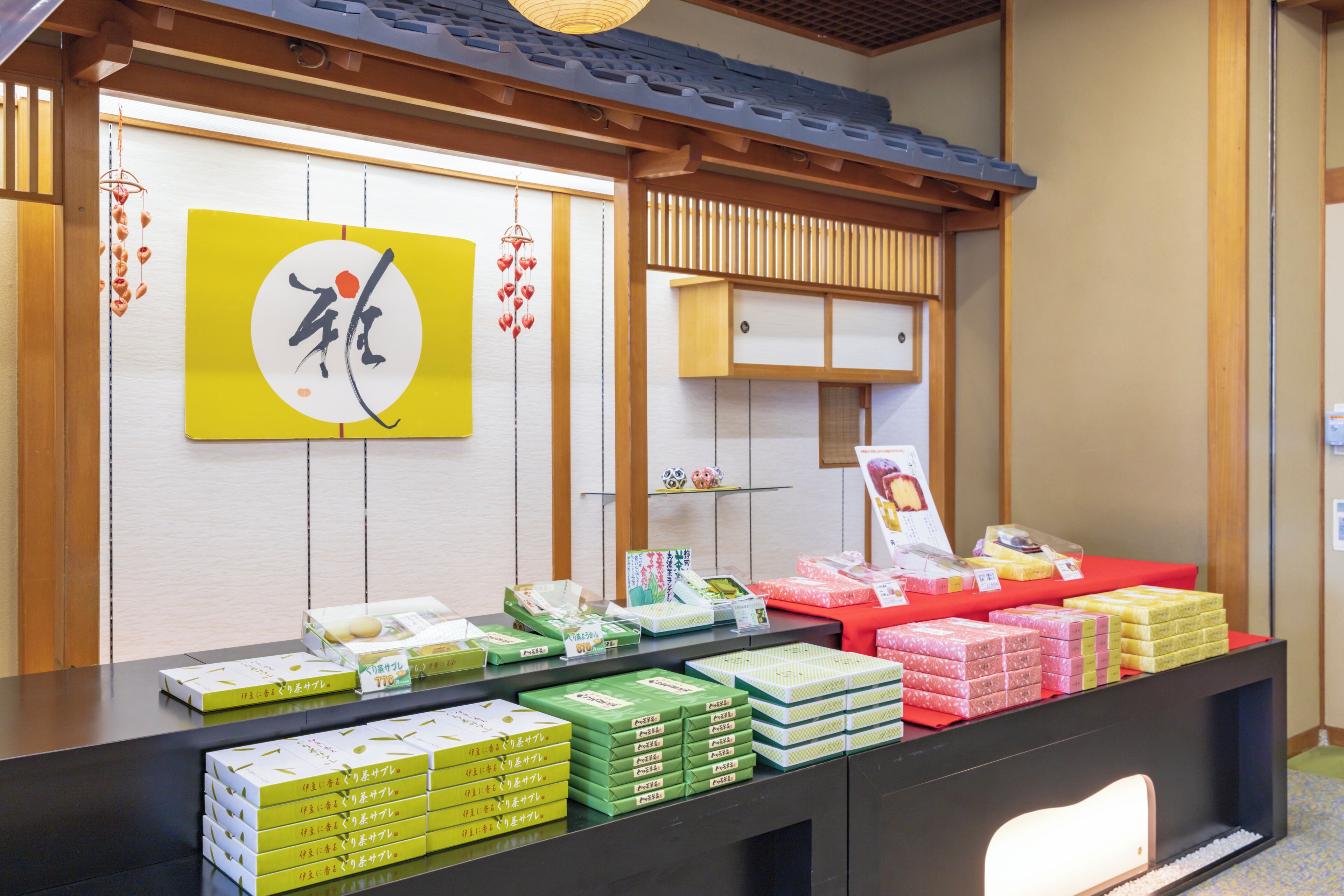 A reception desk with a traditional Japanese aesthetic, featuring a wooden counter, a wall with sliding doors, and a hanging sign with Japanese characters.