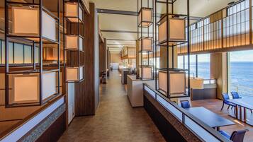 A modern hotel lobby with a long reception desk, wooden paneling, and a view of the ocean.