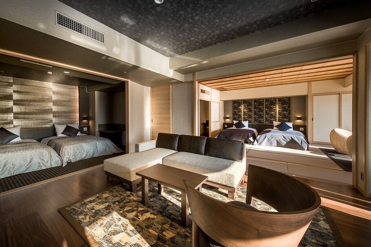 A modern hotel room with a large bed, a sofa, a wooden coffee table, and a large mirror.