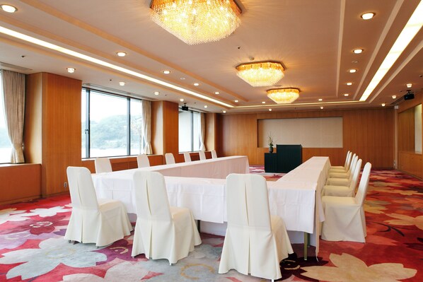 A conference room with a long table, white chairs, chandeliers, and large windows.