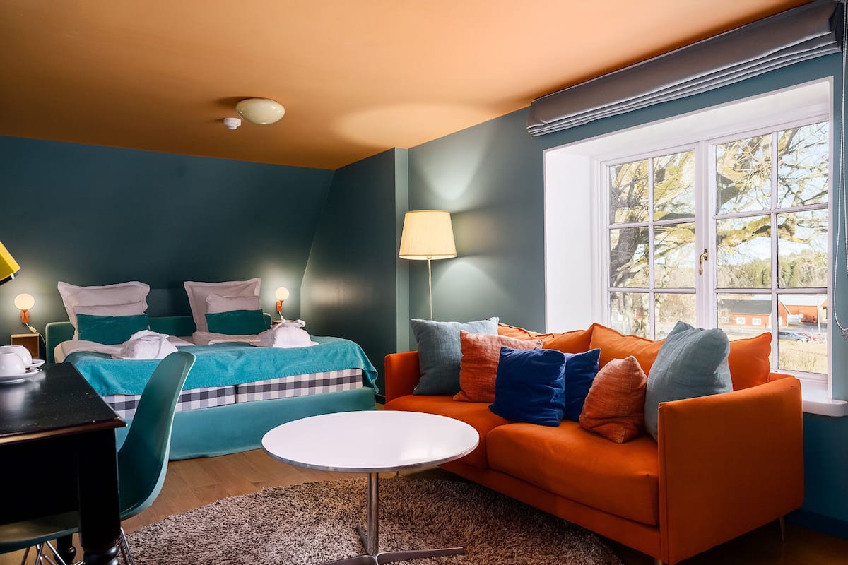 A modern room with teal walls, a teal bed, an orange sofa, and a round white table.