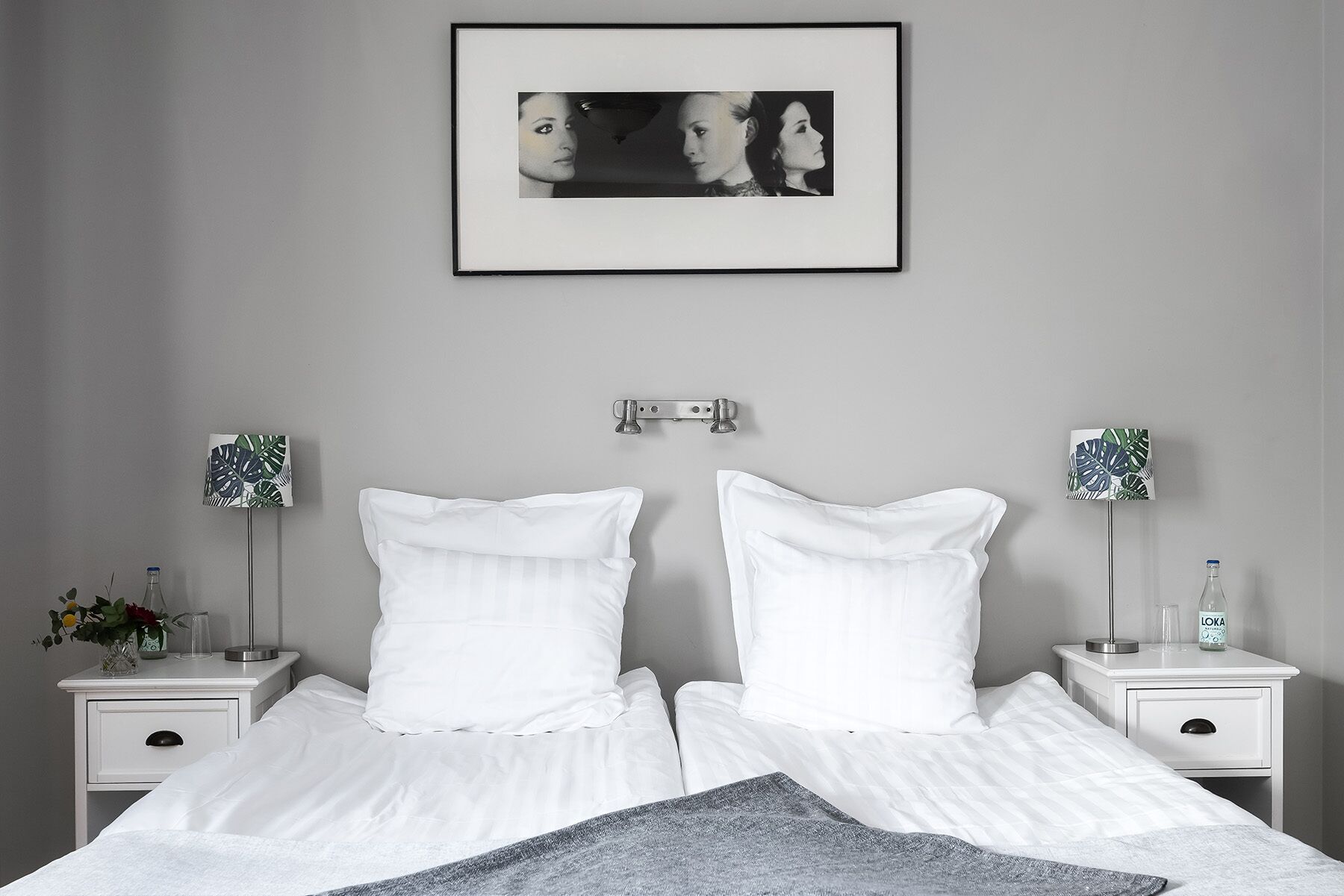 Un dormitorio con una cama, dos mesitas de noche, un cuadro enmarcado y dos lámparas.