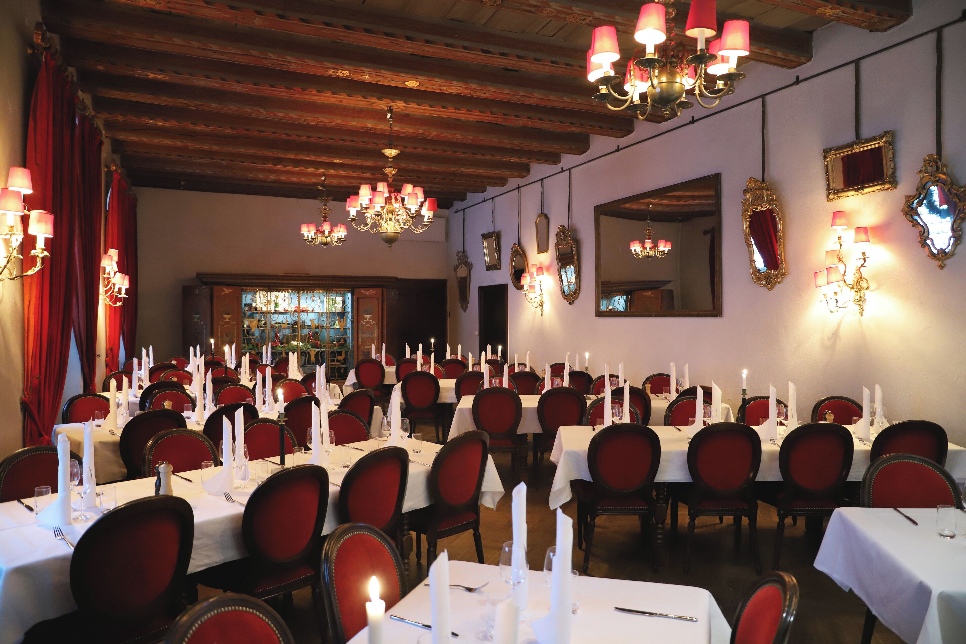Een balzaal met gedekte tafels voor een formeel evenement, met kroonluchters, rode stoelen en wandspiegels.