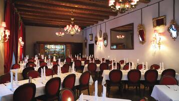 A banquet hall with tables set for a formal event, featuring chandeliers, red chairs, and wall-mounted mirrors.