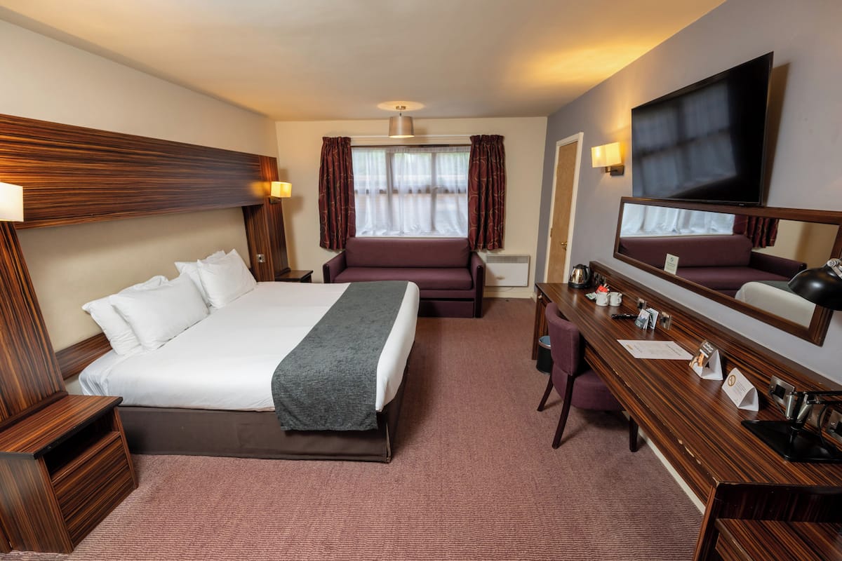 A hotel room with a large bed, a desk with a mirror, a sofa, and a TV.
