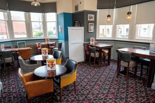 A restaurant interior with tables and chairs, a refrigerator, and large windows.