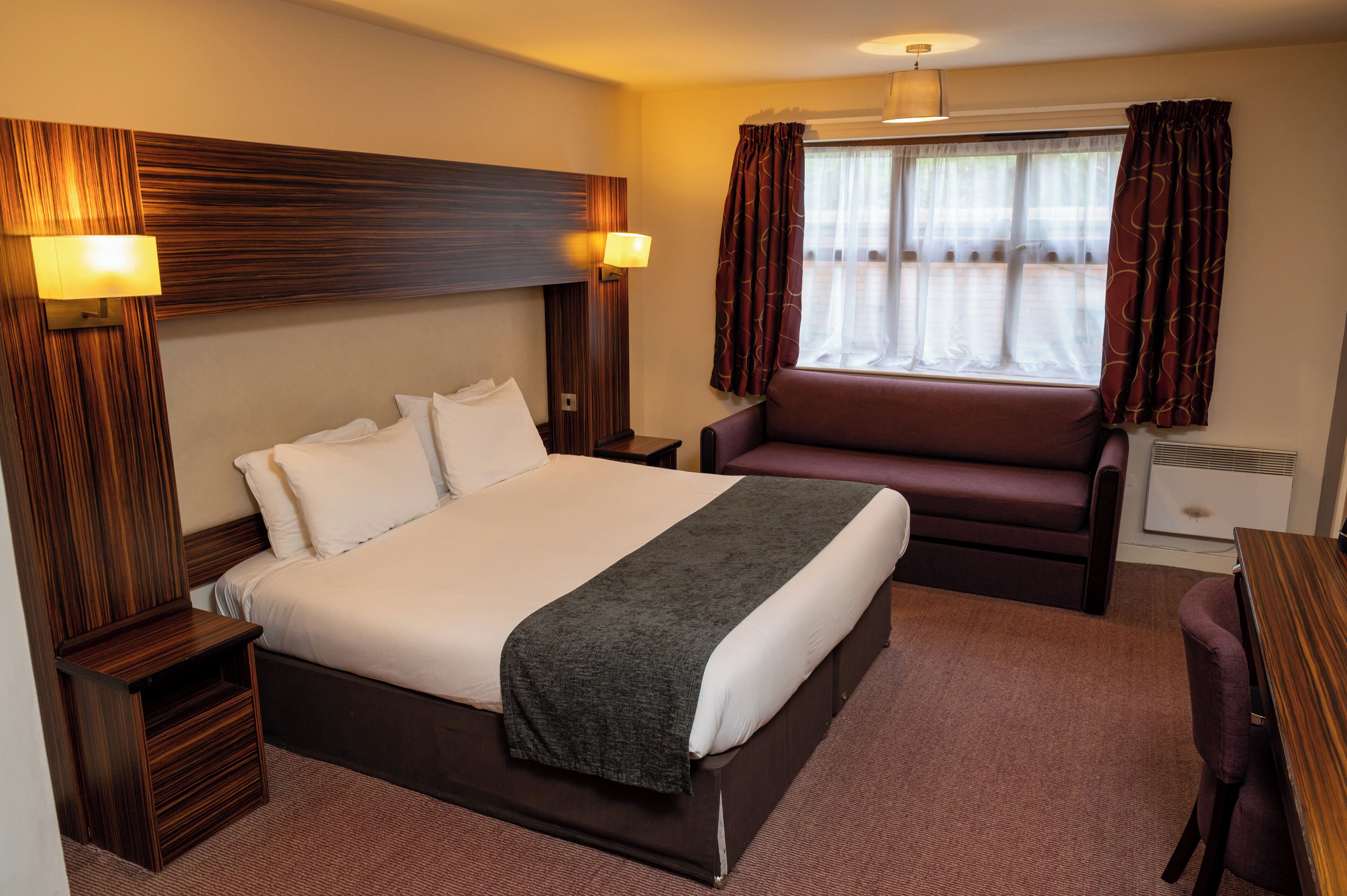 Una habitación de hotel con una cama grande, un cabecero de madera, un escritorio y una silla.
