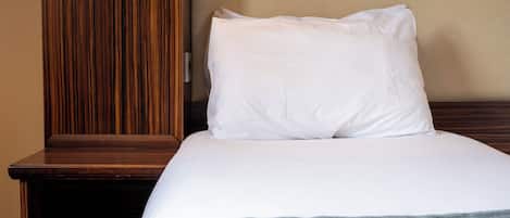 A neatly made bed with white bedding and a gray throw blanket, a wooden nightstand, and a wooden wardrobe.