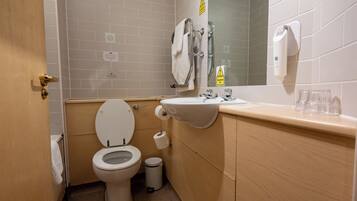 A small bathroom with a toilet, sink, and mirror. There are towels hanging on the wall and a trash can.