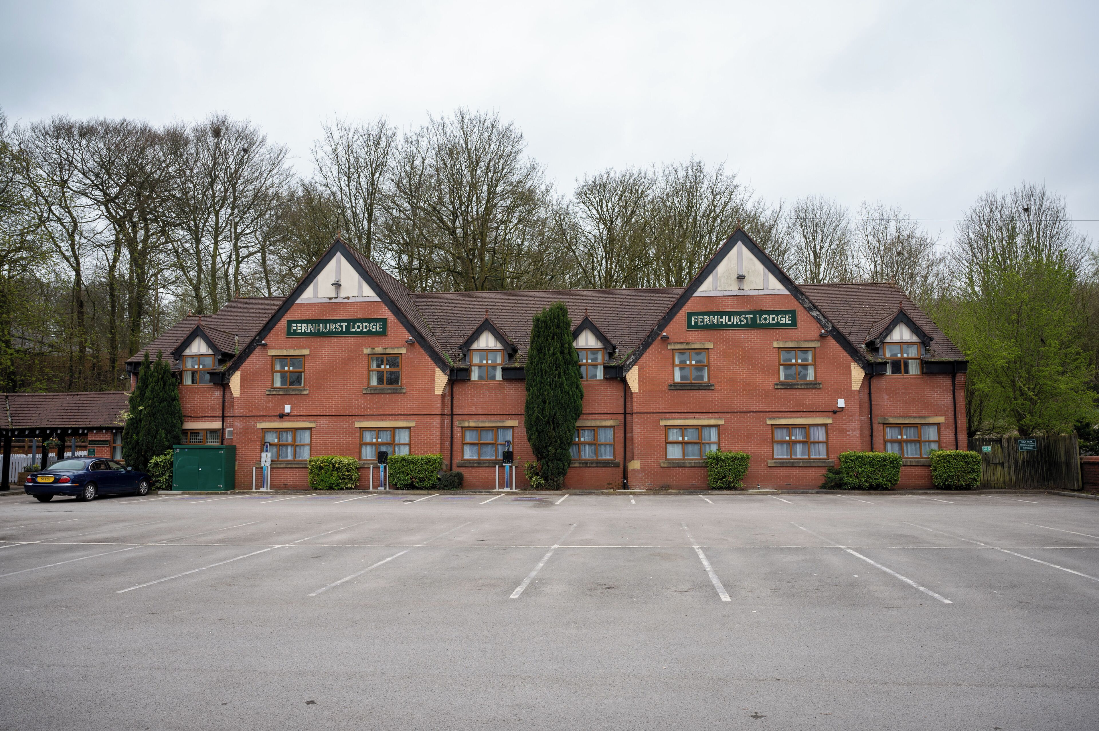 A row of red brick buildings with the name 'Fernhurst Lodge' on the front. There is a parking lot in front of the buildings.