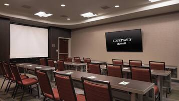 A conference room with multiple tables and chairs, a projection screen, and a sign for Courtyard Marriott.