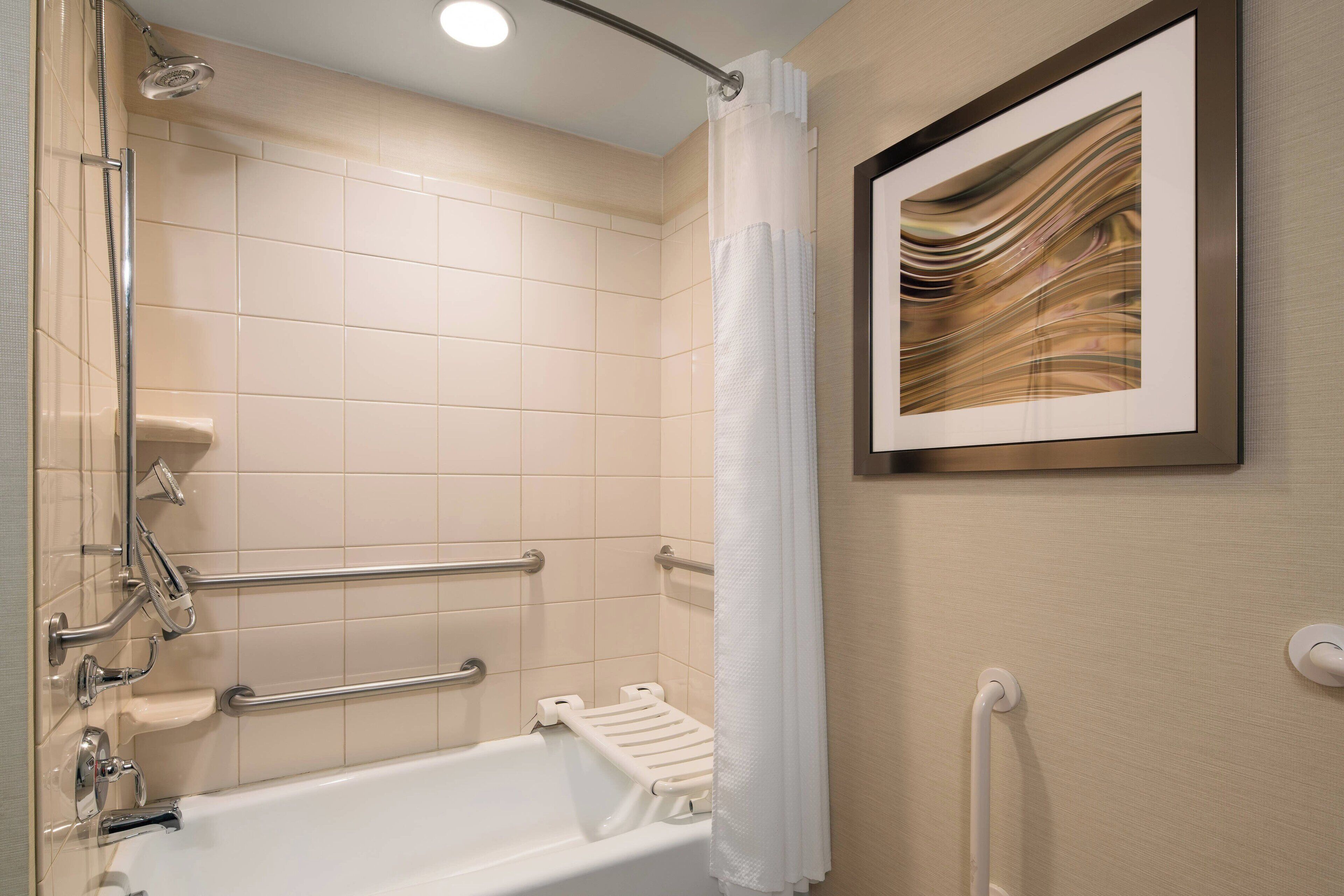 A bathroom with a bathtub, grab bars, a showerhead, and a framed artwork on the wall.