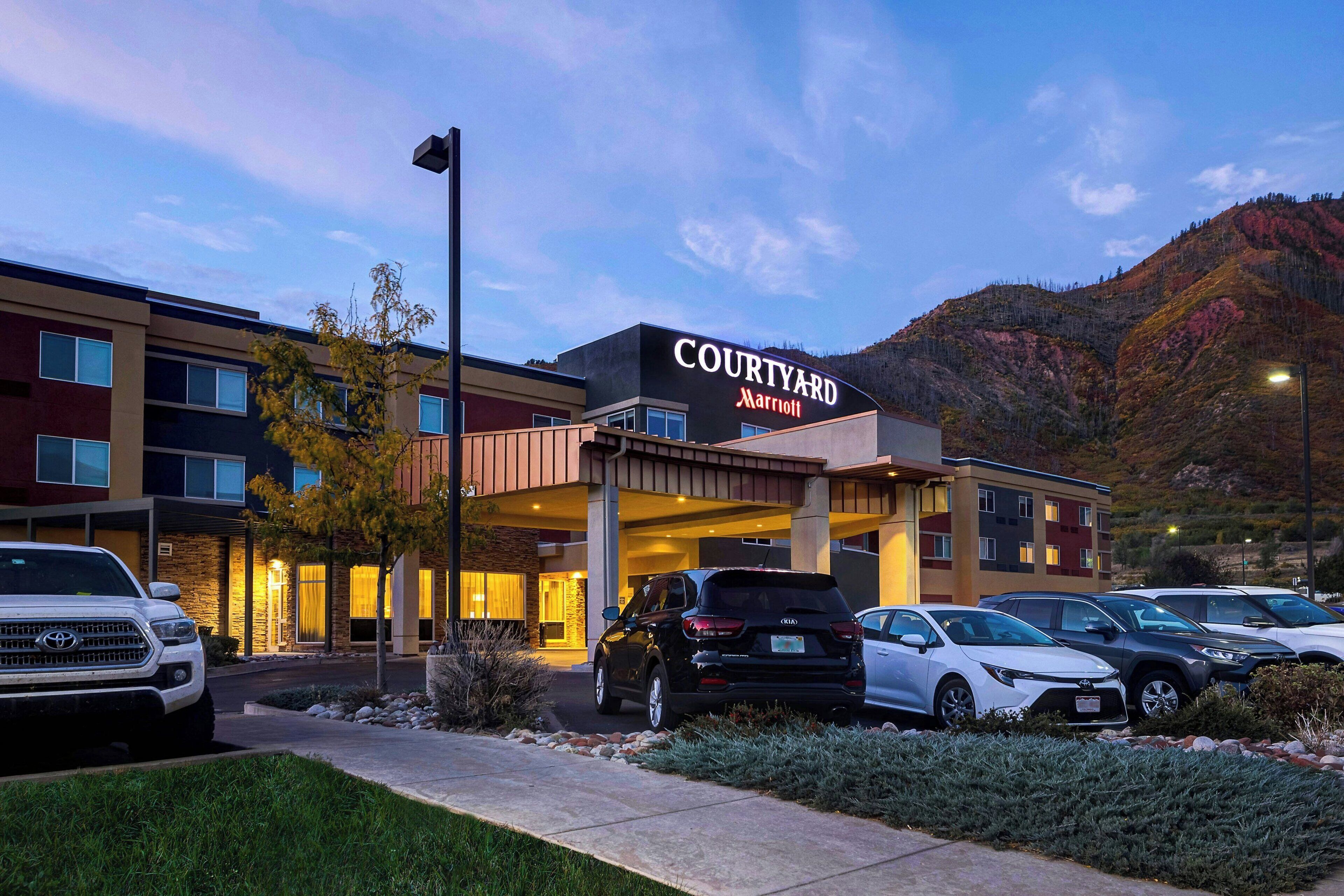 Un hotel Courtyard Marriott con un estacionamiento y montañas al fondo.