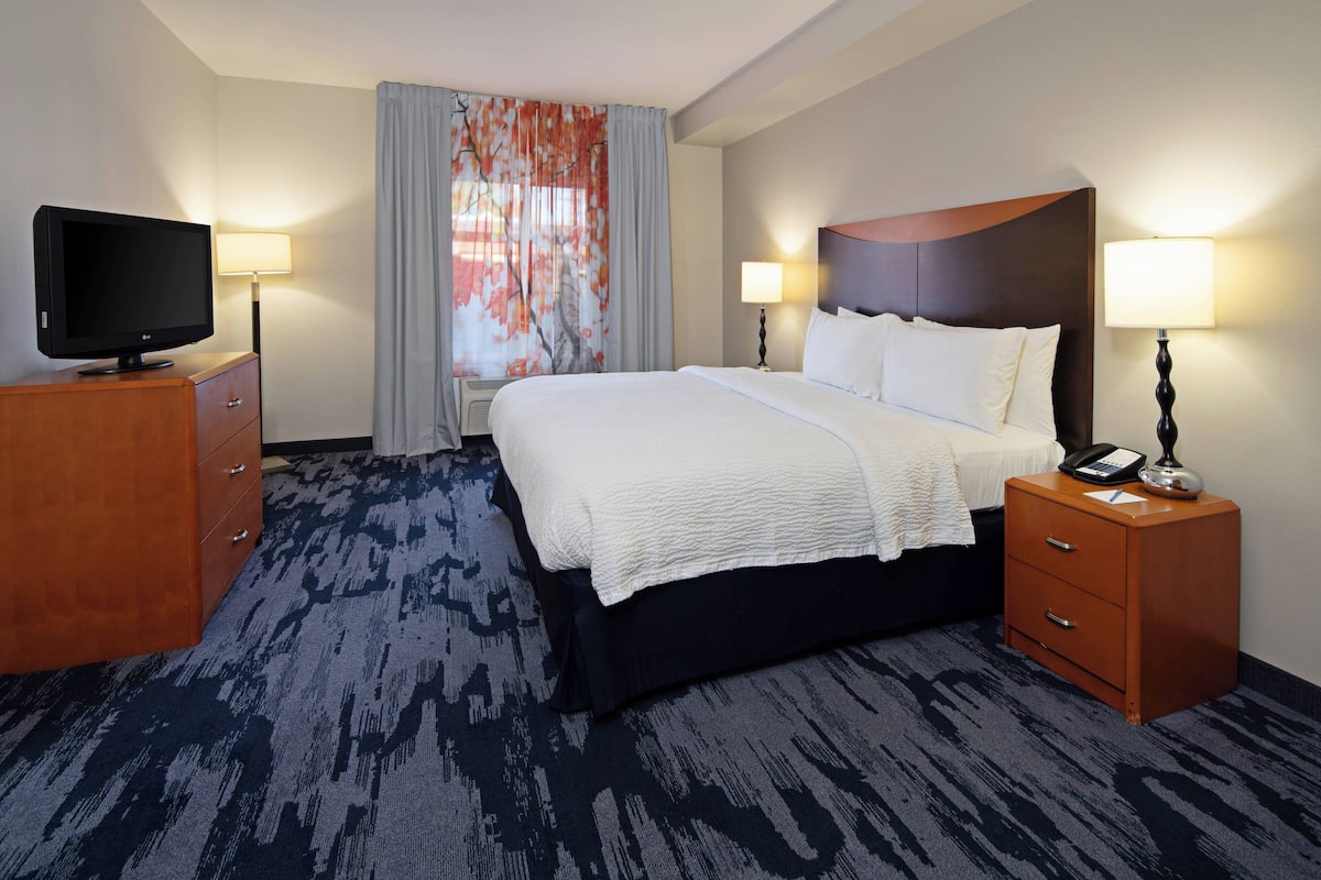 Une chambre d’hôtel avec un grand lit, un téléviseur posé sur une commode en bois et deux tables de chevet avec des lampes.