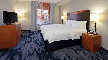 A hotel room with a large bed, a TV on a wooden dresser, and two bedside tables with lamps.