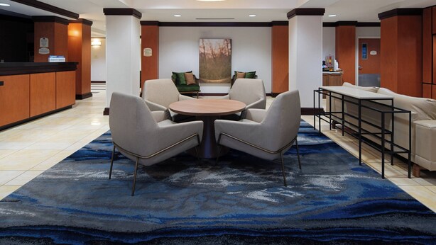 A lobby with a reception desk, a round table with four chairs, a sofa, and a large abstract painting on the wall.