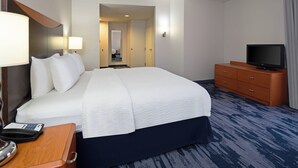 A hotel room with a large bed, a TV on a wooden dresser, a desk with a telephone, and a lamp.