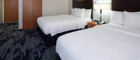 Habitación de hotel con dos camas, un armario y una mesita de noche con lámpara.