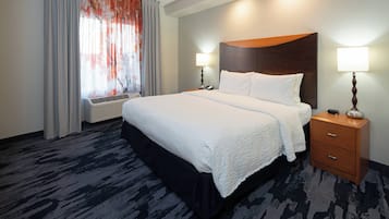Una habitación de hotel con una cama grande, dos mesitas de noche con lámparas, un ventanal con cortinas y suelo cubierto de alfombra.