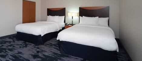 Una habitación de hotel con dos camas, una mesita de noche y una lámpara, y una puerta.
