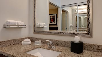 Un baño con encimera de granito, lavamanos, espejo y toallero.