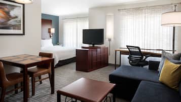 A hotel room with a bed, a TV, a desk, a chair, a sofa, and a lamp.