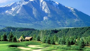 Paisaje montañoso con un campo de golf y una pequeña cabaña.