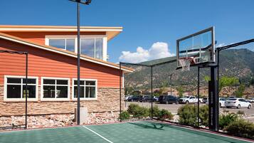 Un terrain de basketball extérieur, situé à côté d’un bâtiment à la façade en pierre et doté de grandes fenêtres.