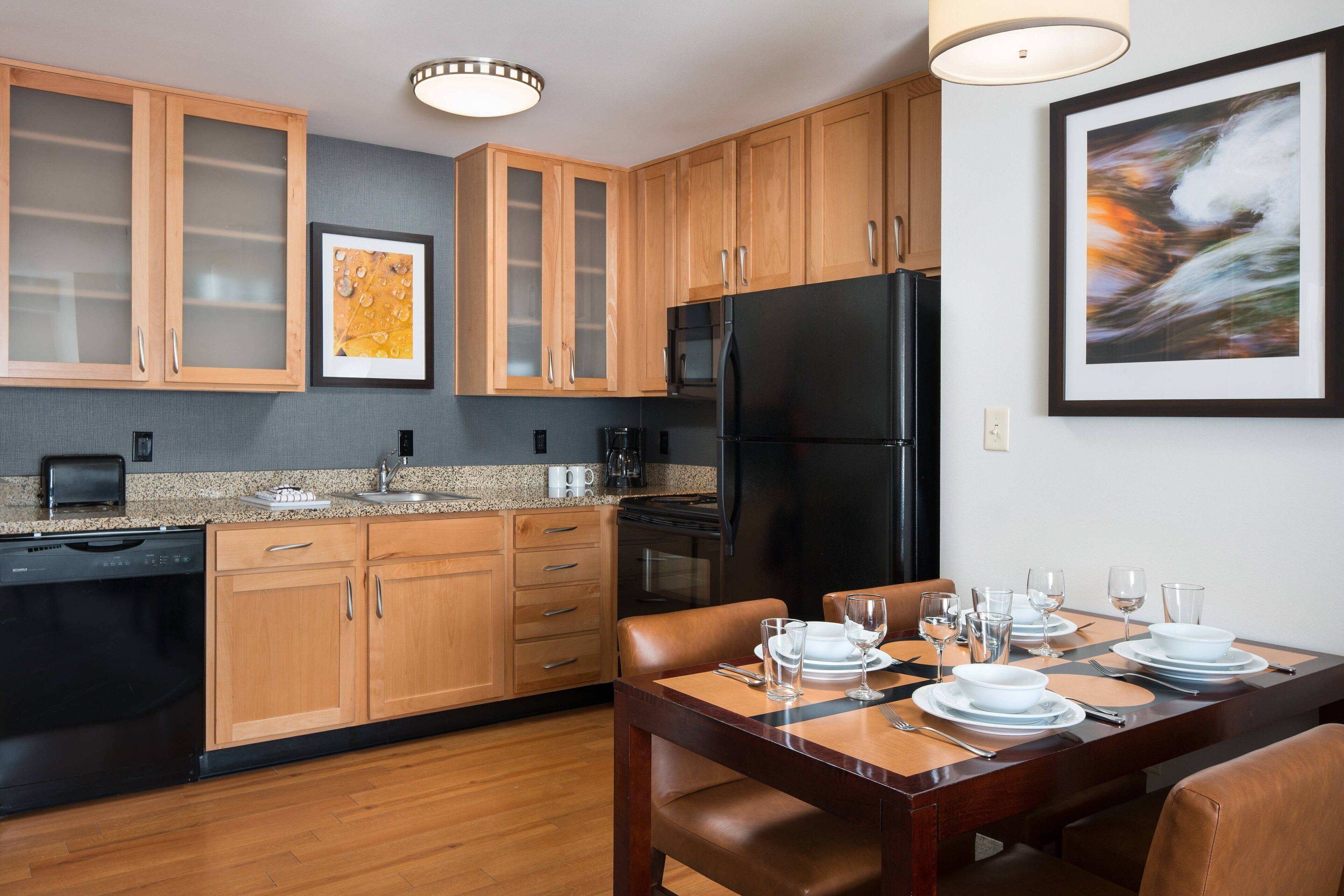 Una cocina moderna con armarios de madera, un refrigerador negro y una mesa de comedor preparada para cuatro comensales.