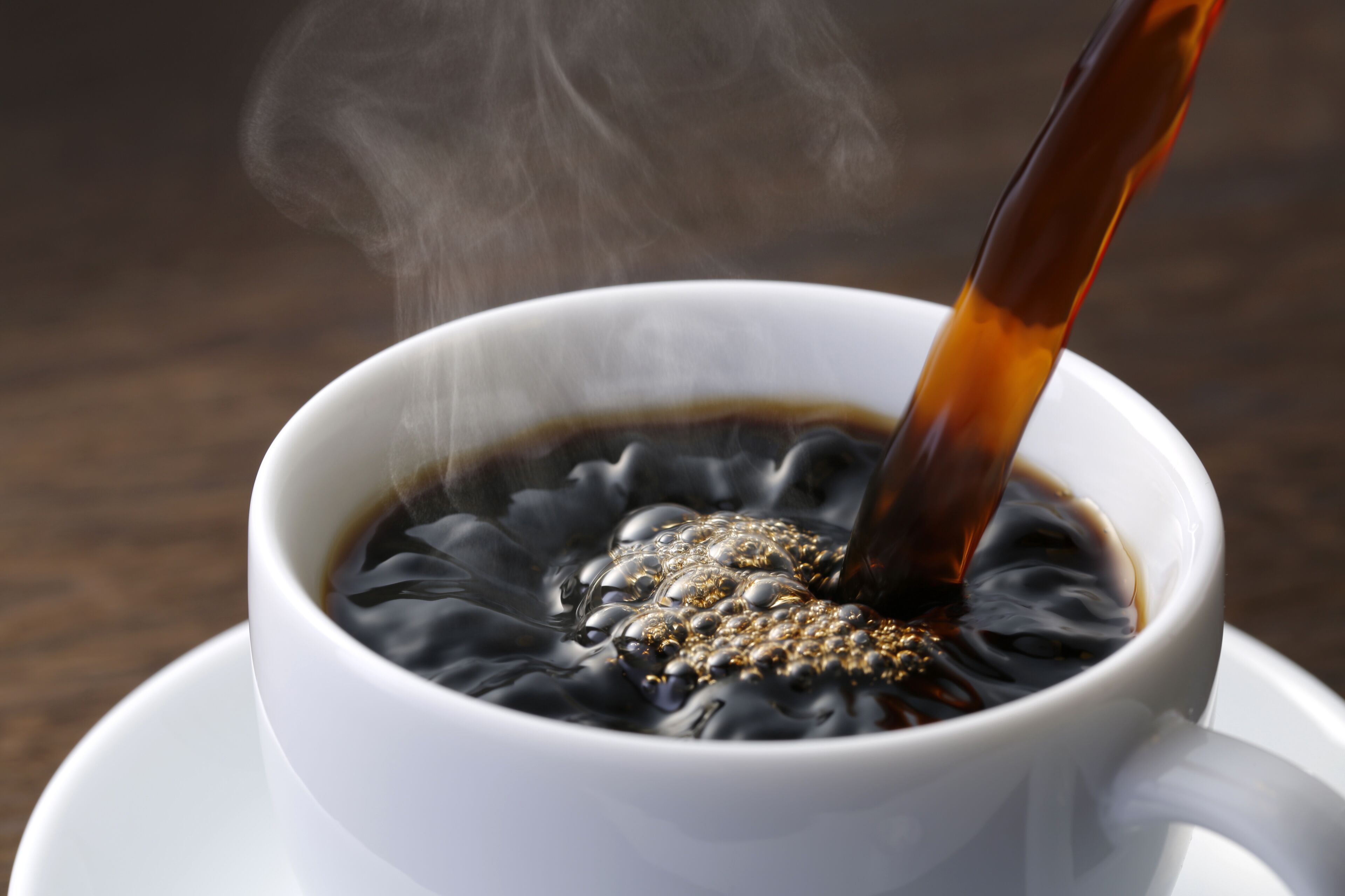 Una taza blanca con café, vapor saliendo de la taza, y una cuchara removiendo la bebida.