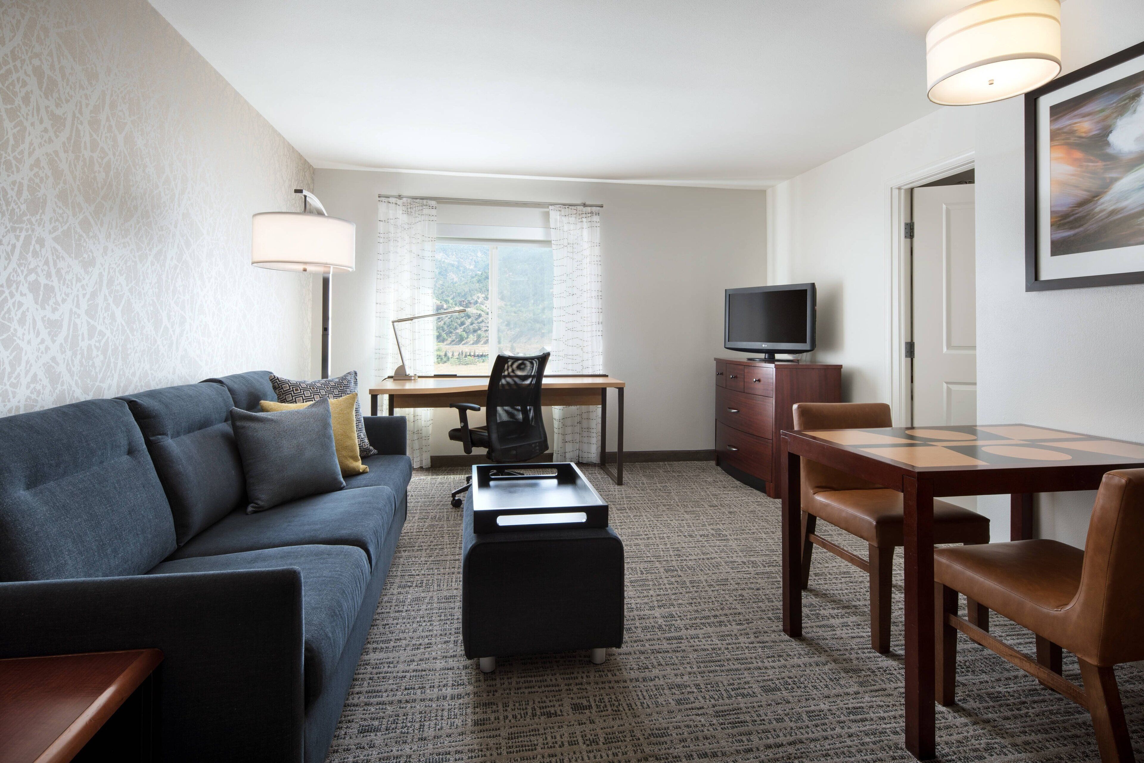 A compact living space with a sofa, a small dining table with chairs, a TV, and a desk with a chair.