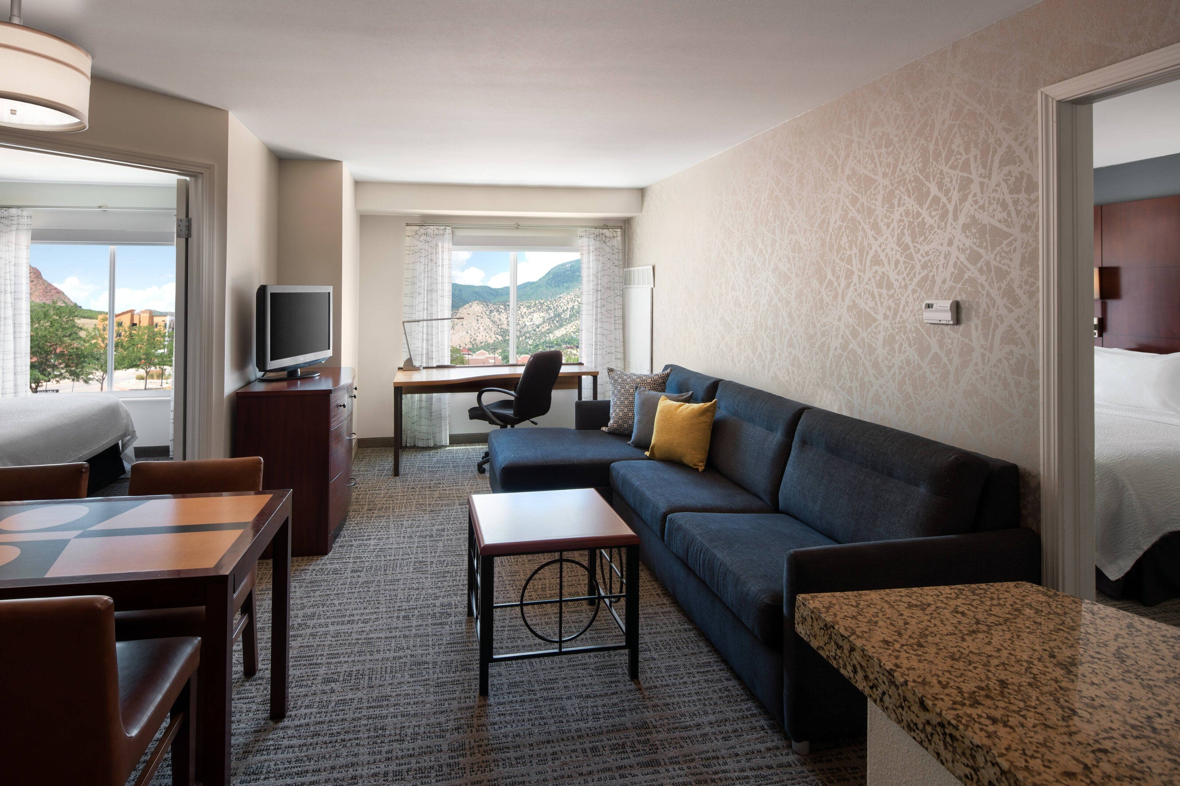 Una habitación de hotel con una cama grande, un sofá, un escritorio con computadora, televisión y vista a las montañas.