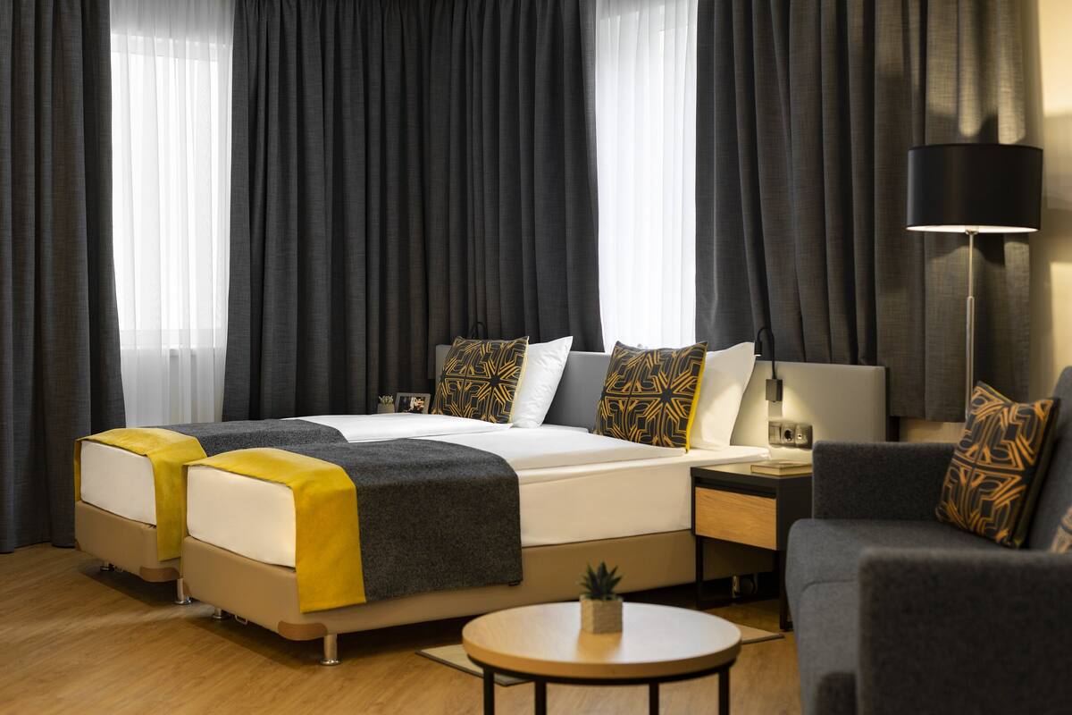Una habitación de hotel moderna con una cama grande, mesitas de noche, un sofá y una lámpara.