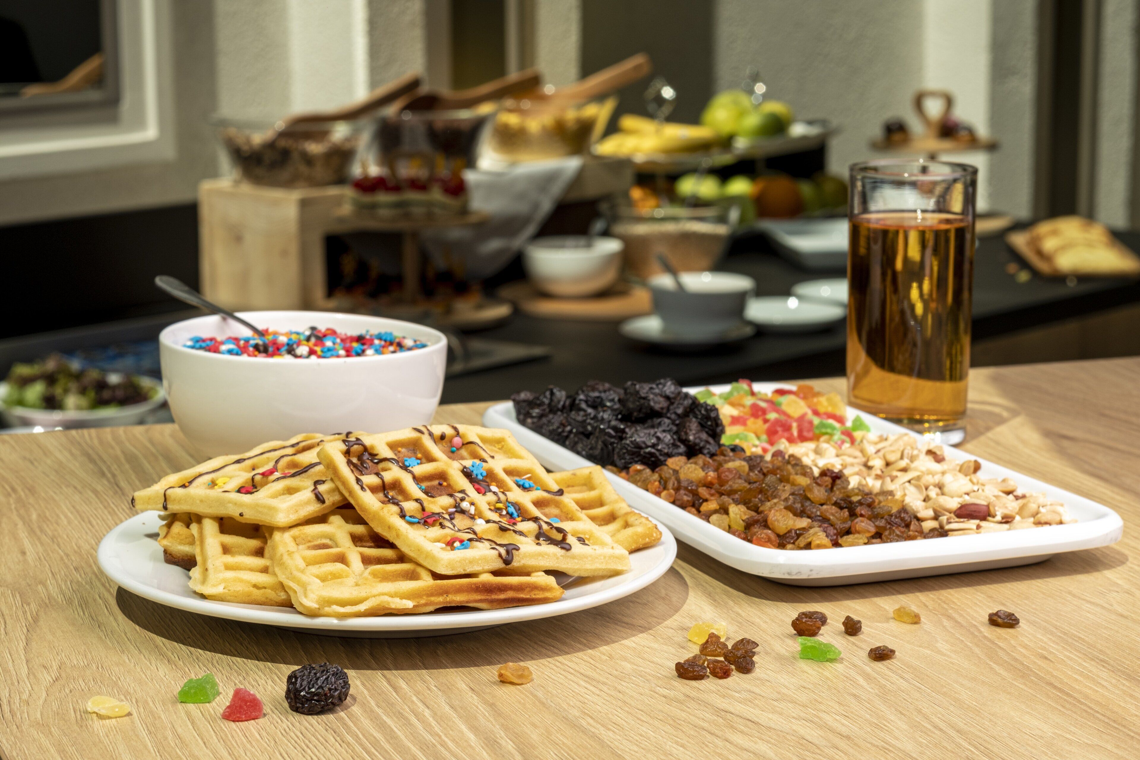 A breakfast buffet with waffles, assorted fruits, and a glass of tea.