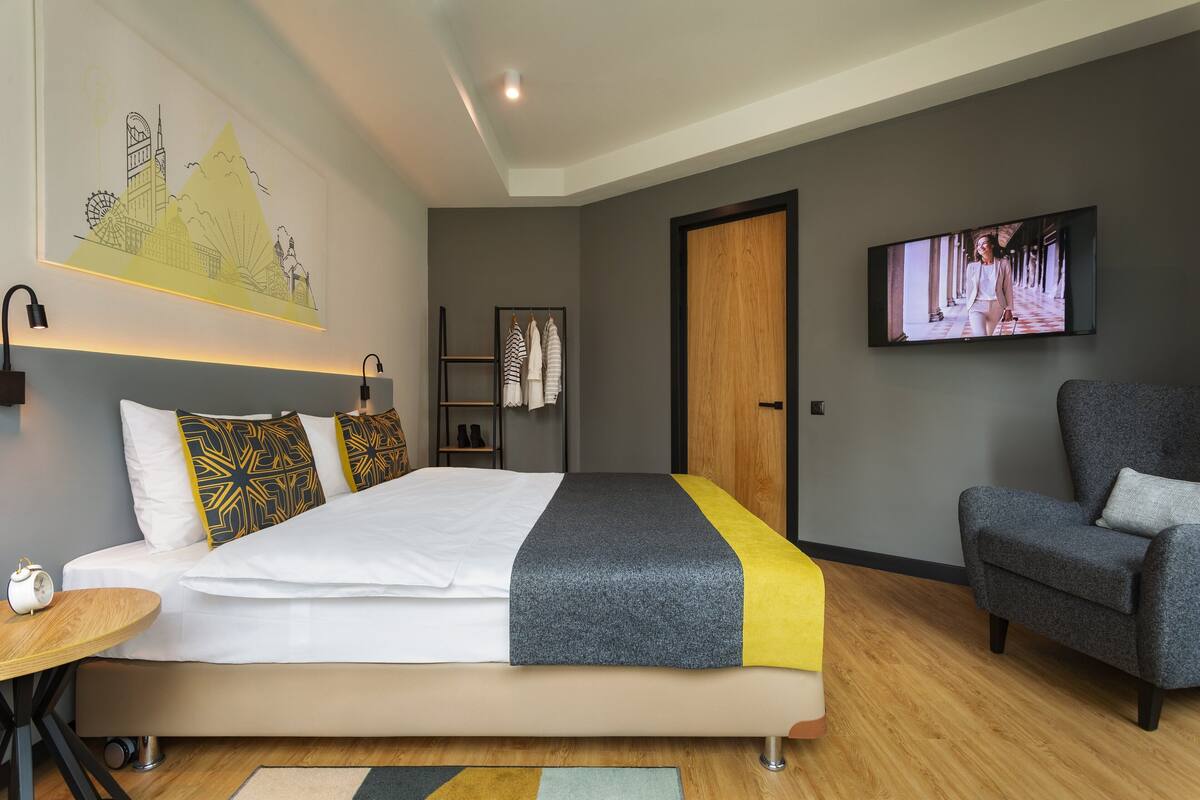 Habitación de hotel moderna con una cama grande, televisor, una silla y estante montado en la pared con toallas.