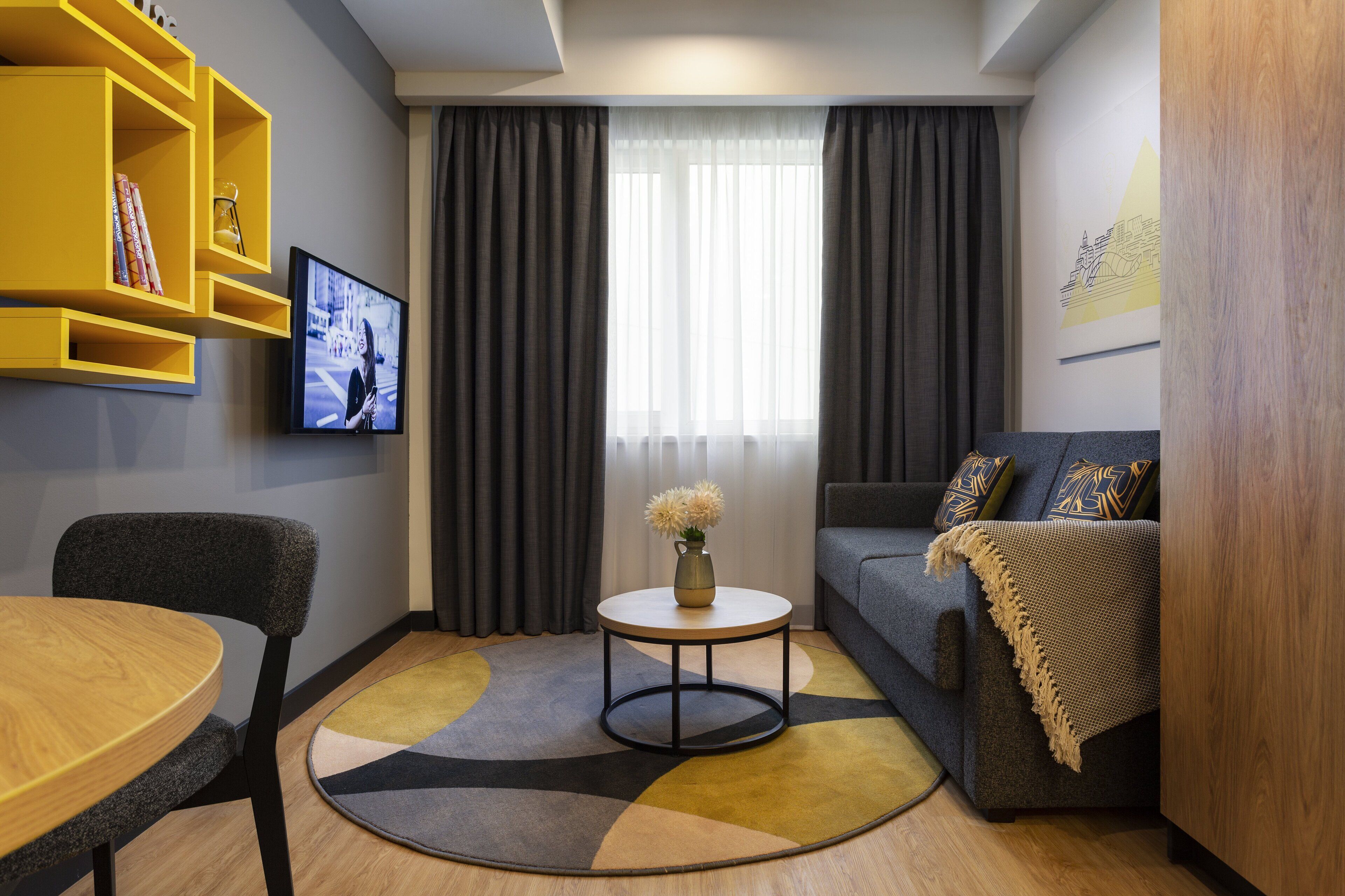 A modern living room with a round coffee table, a sofa, a TV mounted on the wall, and a bookshelf.