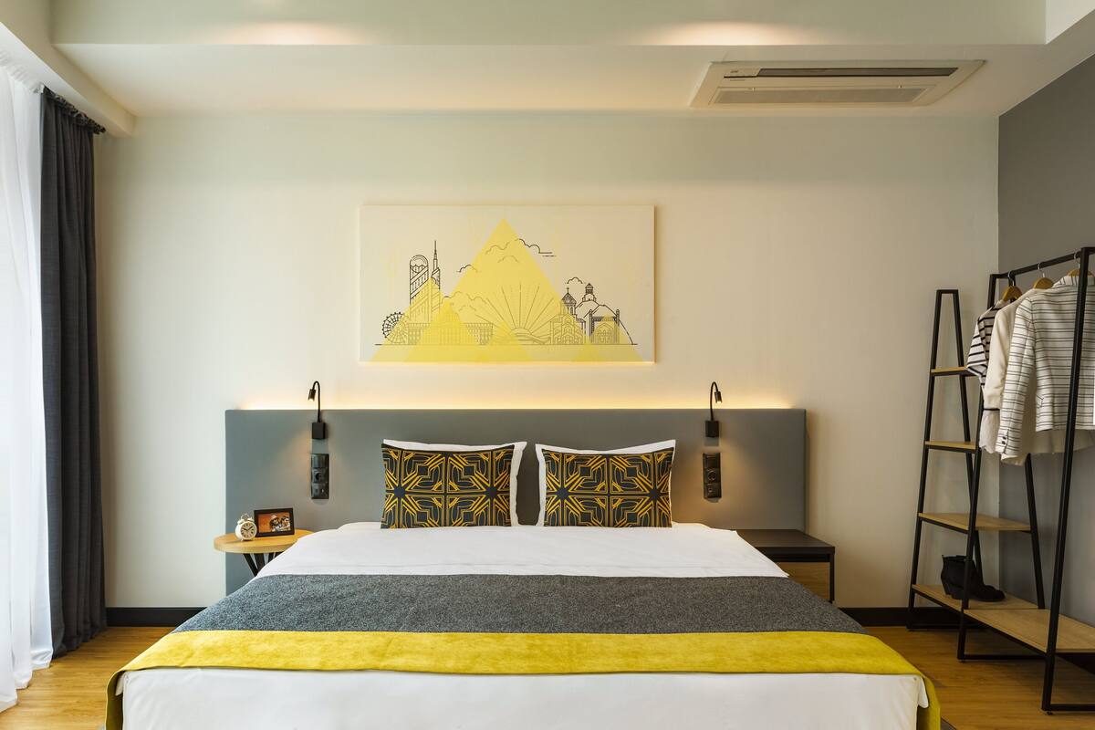 Una habitación de hotel con cama, mesita de noche, un cuadro enmarcado en la pared y un perchero.