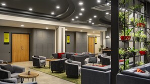 A modern lounge area with sofas and armchairs, a coffee table, and a vertical plant wall. - The Gate Hotel City Centre (Tbilisi)