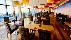 Un restaurante amplio con techos altos, ventanas grandes y mobiliario moderno.