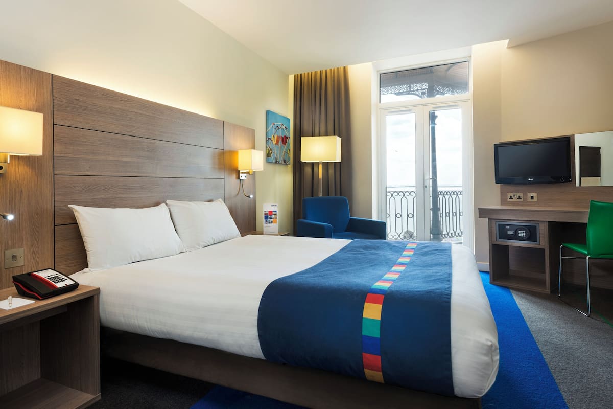 Habitación de hotel con una cama grande, lámparas de noche, un escritorio con una computadora y vistas al balcón exterior.
