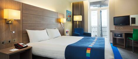 A hotel room with a large bed, bedside lamps, a desk with a computer, and a view of the outside balcony.